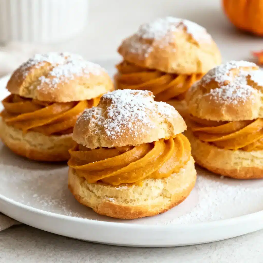 Golden pumpkin spice cream puffs filled with silky pumpkin cream, dusted with powdered sugar