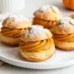 Golden pumpkin spice cream puffs filled with silky pumpkin cream, dusted with powdered sugar