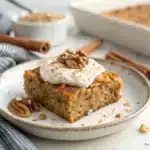 A perfect, close-up square of high protein carrot cake baked oatmeal, topped with protein cream cheese frosting and walnuts on a white plate.