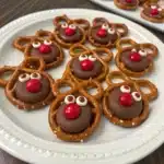 A plate of reindeer pretzels made using Hershey Kisses instead of Rolos, with a red M&M nose pressed into the center.