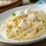 Close up of fettuccine noodles coated in thick cottage cheese alfredo sauce.