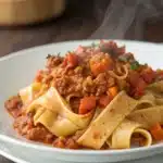 Close-up macro of glistening turkey bolognese sauce clinging to wide pappardelle pasta on a white ceramic plate.