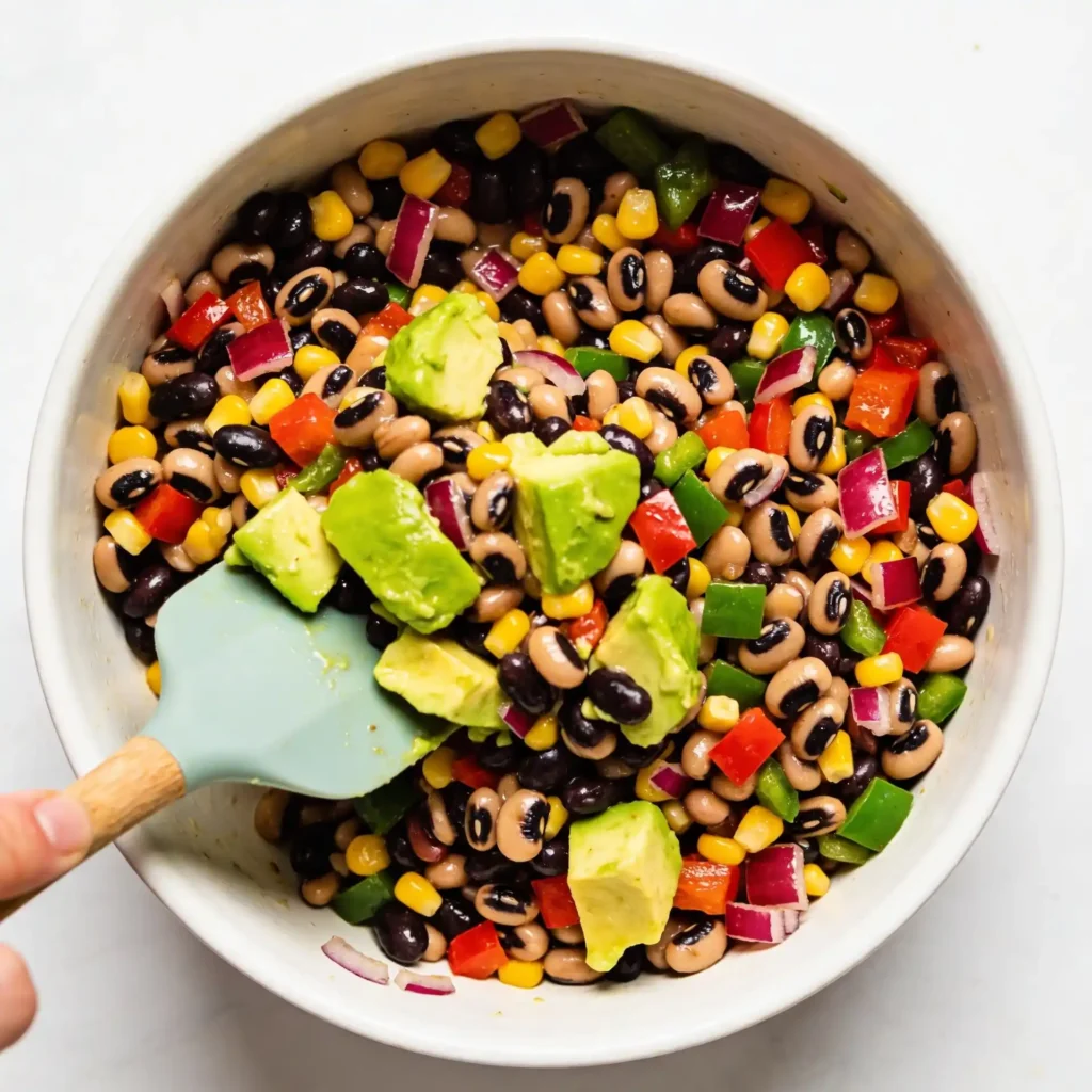 Folding avocado into a high protein cowboy caviar salad.