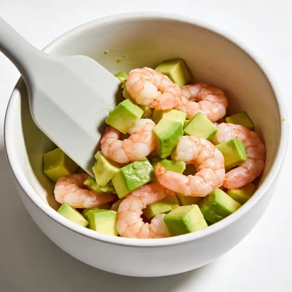 Gently folding diced avocado cubes into a shrimp and lime salad base.