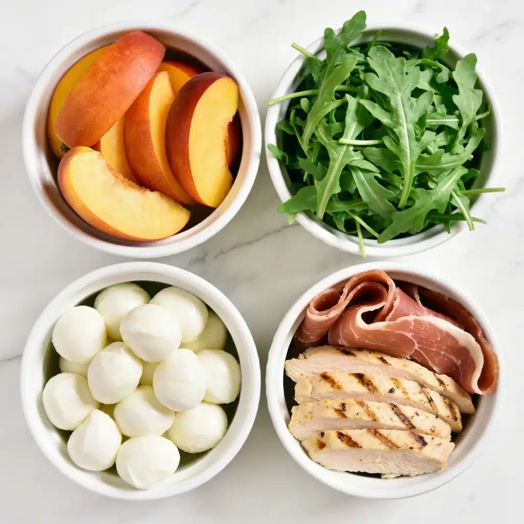 Fresh ingredients spread for a peach and prosciutto salad on a marble surface.