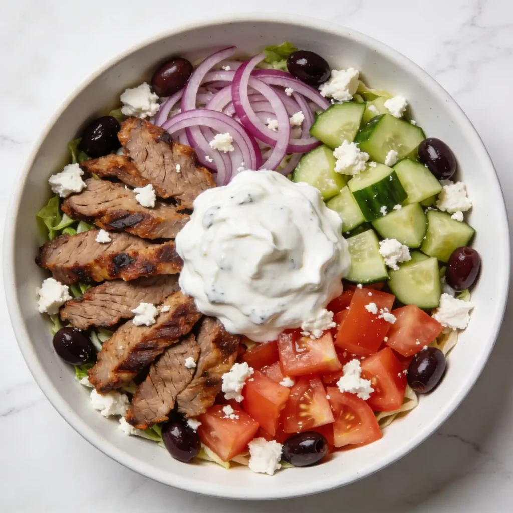 A vibrant Greek Gyro Salad in a white bowl with seared meat and Tzatziki.