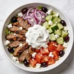 A vibrant Greek Gyro Salad in a white bowl with seared meat and Tzatziki.
