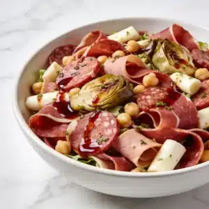 A finished High Protein Italian Antipasto Salad in a white bowl with marinated vegetables and lean meats.