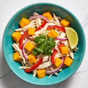 A vibrant Mango Lime Shredded Chicken Salad in a turquoise bowl on a marble table.