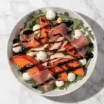 A vibrant Peach and Prosciutto Salad with grilled peaches and chicken on a white plate.