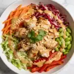 A vibrant Thai Peanut Chicken Salad in a white bowl with creamy peanut dressing.