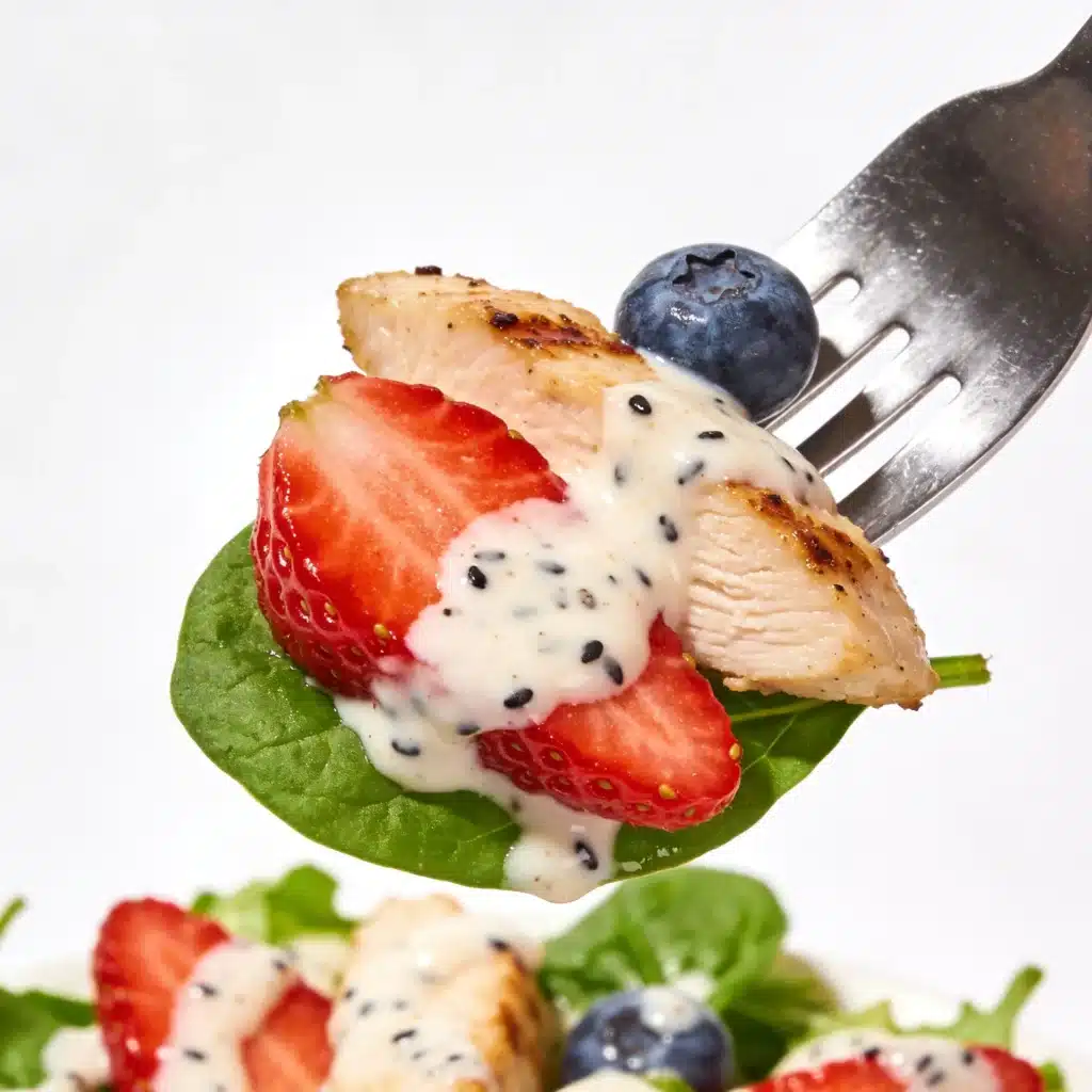 Close up of a fork with chicken, strawberry, and dressing.