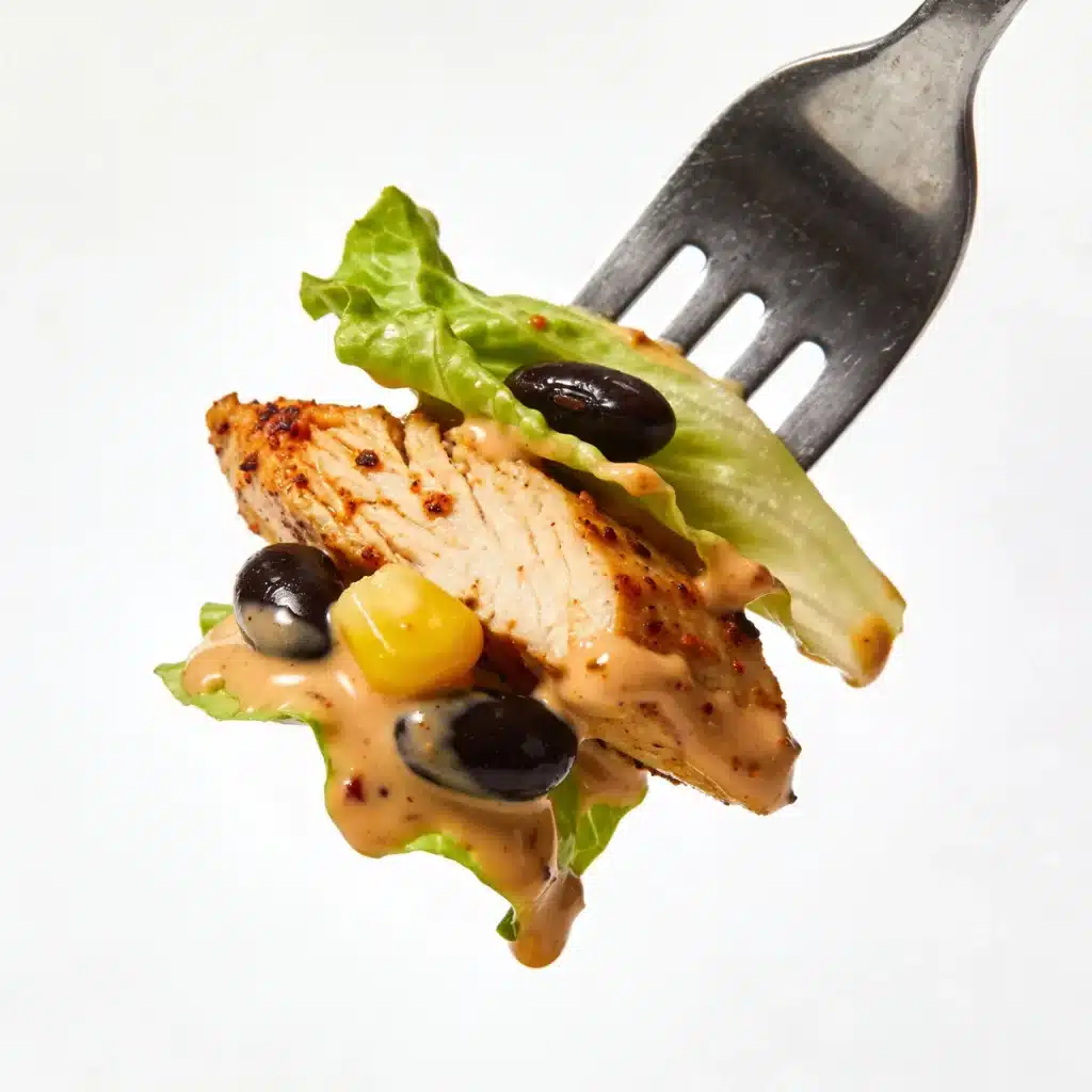 Close up of a fork with chicken, beans, and corn.