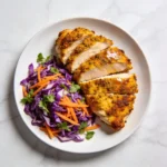 Sliced cumin-rubbed air fryer chicken breast with a colorful rainbow slaw on a white plate.