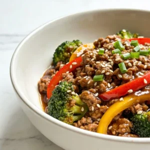 A white bowl featuring a healthy Ginger Garlic Ground Turkey Stir-fry garnished with green onions and sesame seeds.