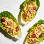 Top-down view of three butter lettuce wraps filled with vibrant yellow Healthy curry chicken salad on a white marble surface.
