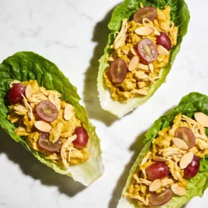 Top-down view of three butter lettuce wraps filled with vibrant yellow Healthy curry chicken salad on a white marble surface.