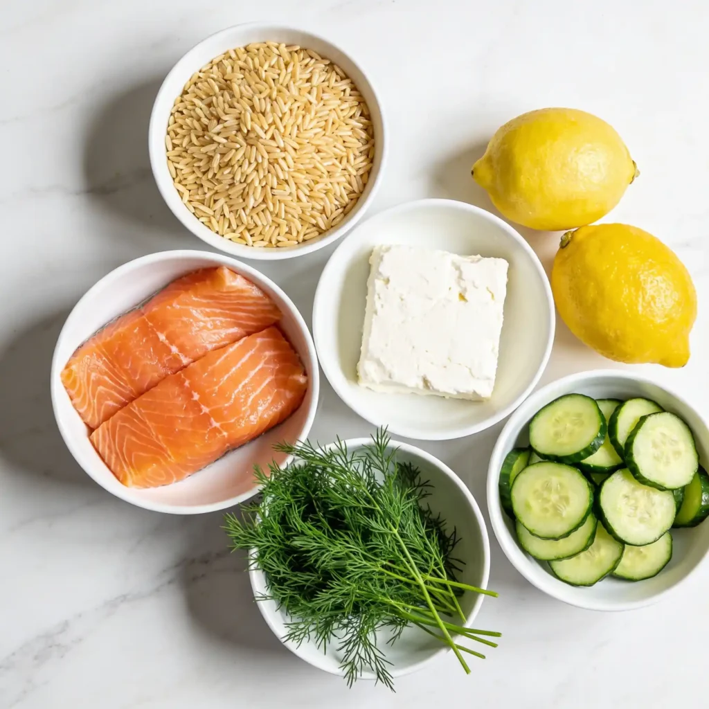 Fresh ingredients for a salmon and orzo salad spread on a marble surface.