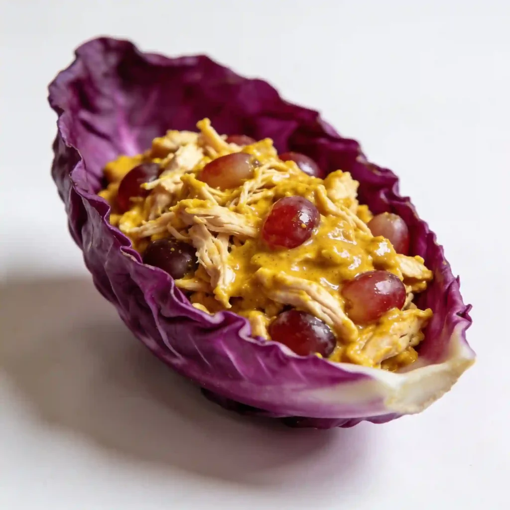 Bright yellow curry chicken salad served inside deep purple cabbage leaves on a white marble board.