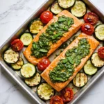 A sheet pan featuring pesto-topped salmon fillets with zucchini and tomatoes.