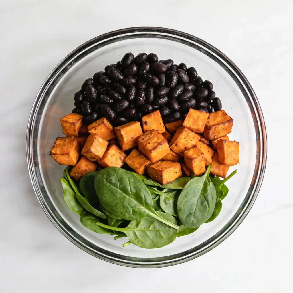 Layering ingredients for a high protein sweet potato bowl.