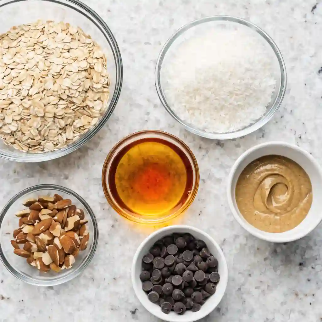 Small bowls filled with rolled oats, coconut, almonds, almond butter, and chocolate chips.