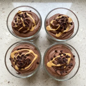 Four small glass tumblers filled with creamy swirled Chocolate Peanut Butter Cottage Cheese Mousse drizzled with peanut butter on a quartz counter.
