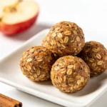 A cluster of healthy apple cinnamon energy balls served on a sleek rectangular white plate.