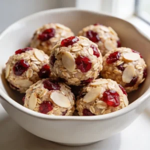 A white bowl of no bake cranberry almond energy bites speckled with red cranberries.