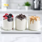 Three glass jars of vanilla cottage cheese mousse, each featuring different toppings like berries and chocolate, on a white tray.