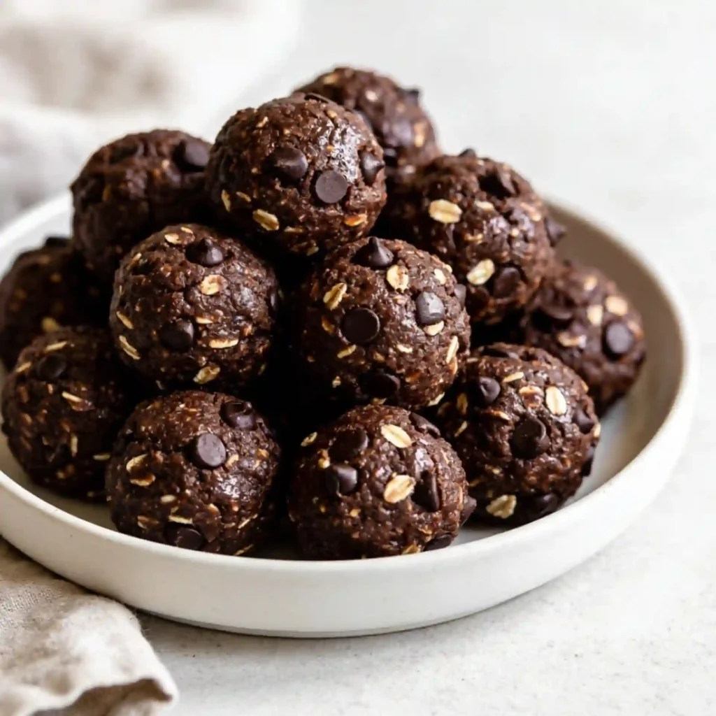 A matte ceramic plate featuring a neat stack of fudgy, dark Double Chocolate Energy Bites studded with mini chocolate chips.