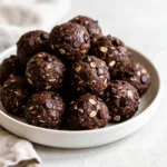 A matte ceramic plate featuring a neat stack of fudgy, dark Double Chocolate Energy Bites studded with mini chocolate chips.