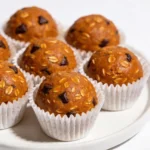 A small cluster of smooth pumpkin spice bites in white cupcake liners on a glossy white surface with a cinnamon stick.