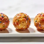 Three healthy cake batter energy balls served on a sleek rectangular white plate.