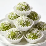 A small cluster of smooth matcha green tea bites in white cupcake liners on a glossy white surface.