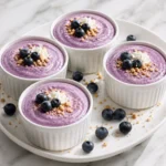 Four white ceramic ramekins filled with smooth purple blueberry cottage cheese mousse, arranged on a glossy white platter with fresh blueberries.