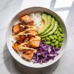 A top-down view of high protein salmon rice bowls featuring seared salmon, avocado, edamame, and rice.