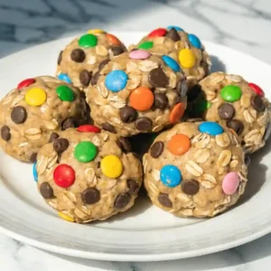 A bowl of no bake monster cookie protein balls with oats and colorful candies.