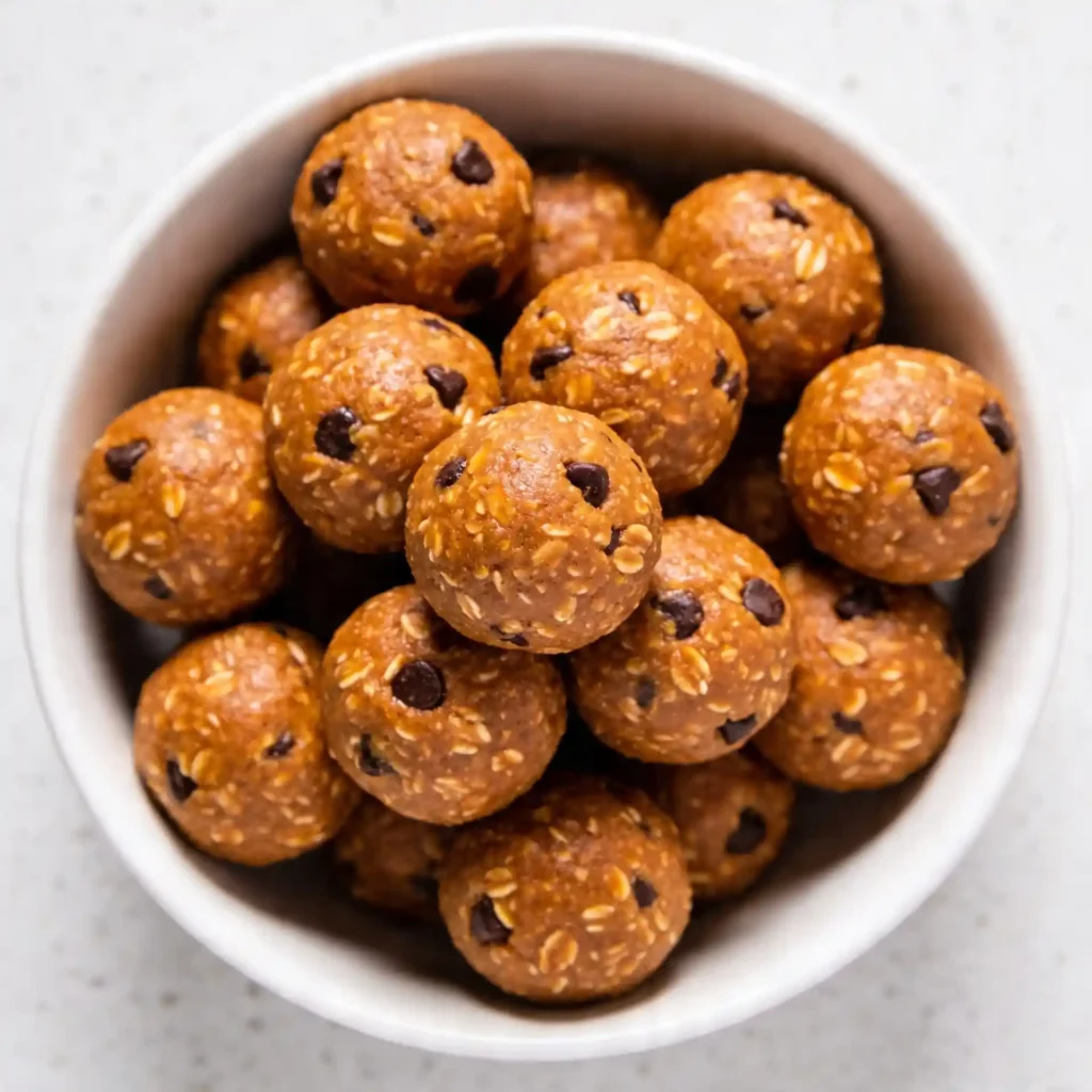 An overhead view of a modern white bowl filled with Pumpkin Spice Protein Balls, styled with a white pumpkin and cinnamon sticks.