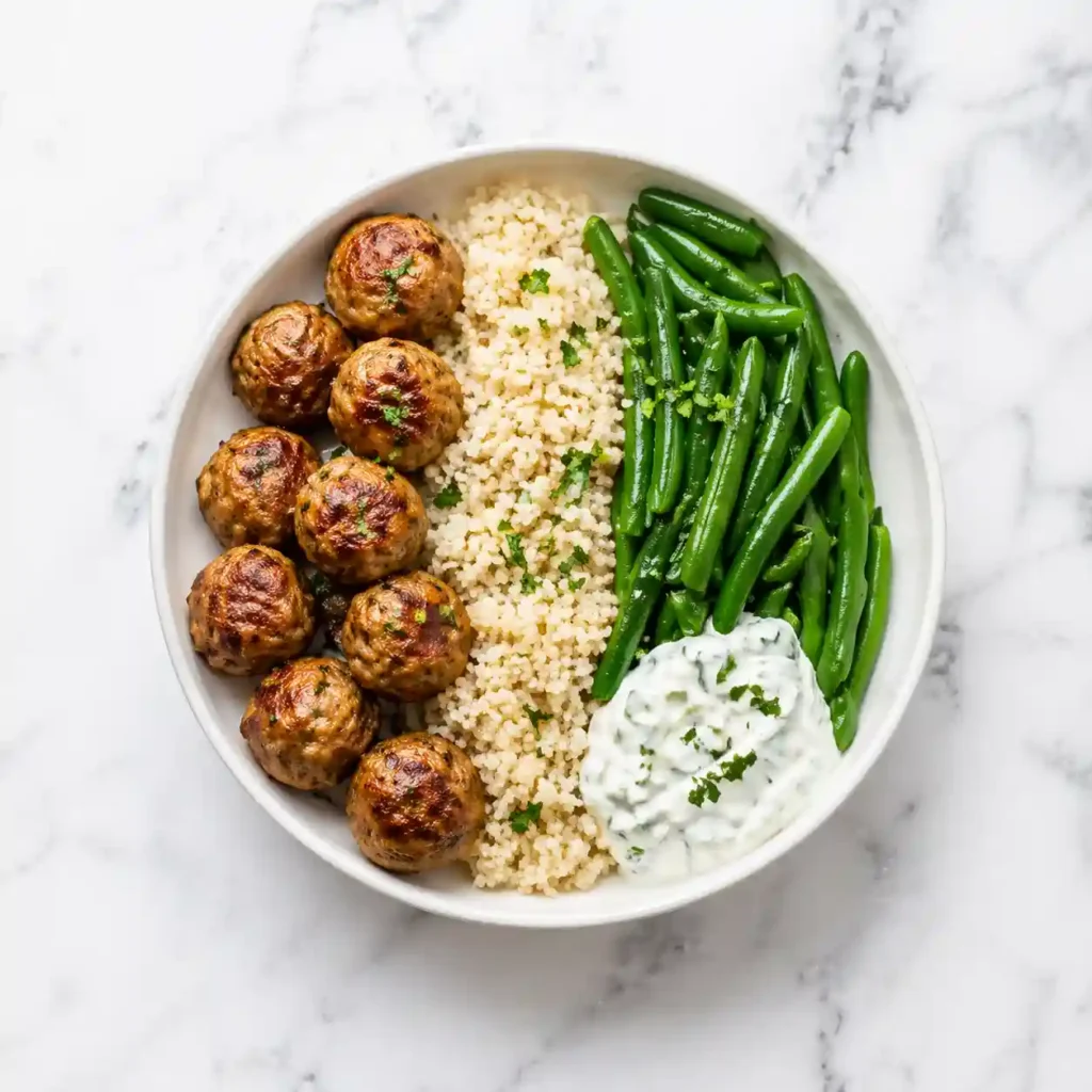 A top-down view of a turkey meatball meal prep bowl featuring baked meatballs, quinoa, and green beans.