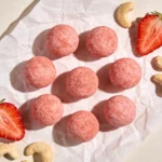 Vegan strawberry energy bites resting neatly on a serving platter with parchment paper.