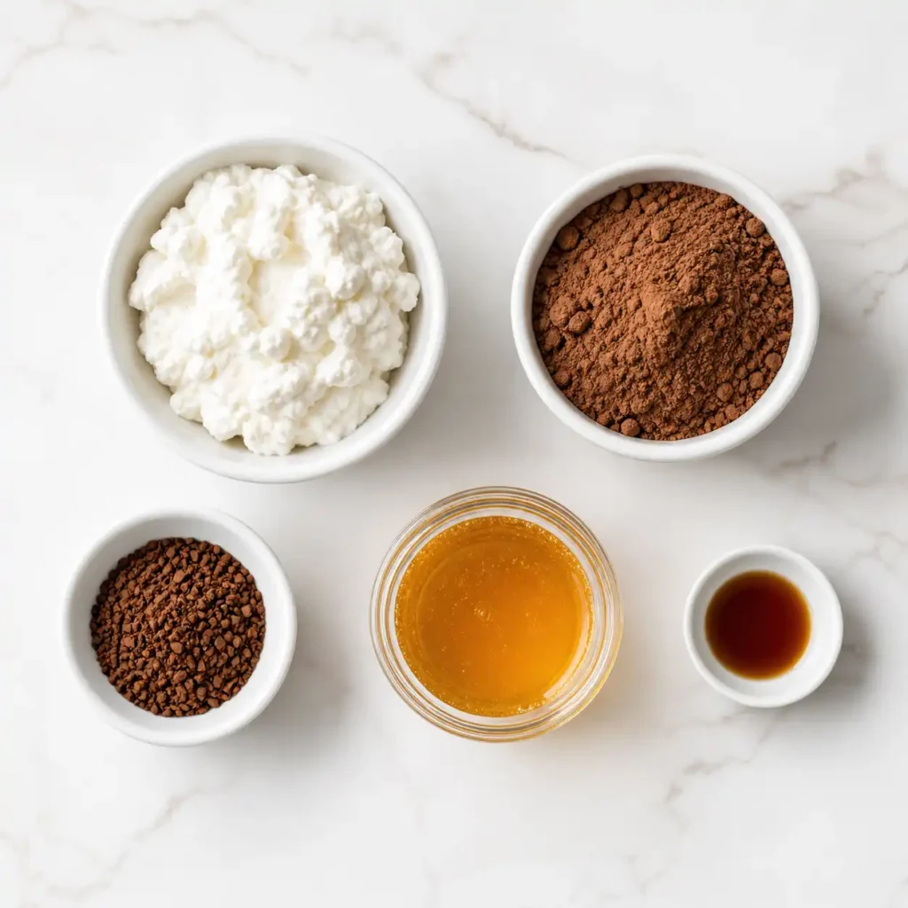 Raw ingredients including cottage cheese, cocoa, and espresso powder arranged in white bowls on a marble surface.