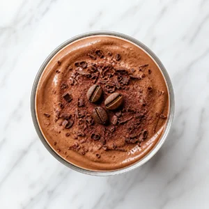A top-down flat lay view of a glass cup filled with silky mocha cottage cheese mousse on white marble.