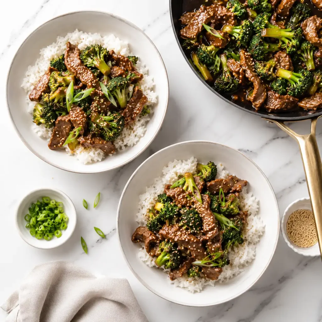 A top-down flat lay of two freshly assembled beef and broccoli dinner bowls on a white marble counter.